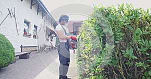Caucasian man in overalls and safety mask cutting bushes