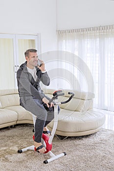 Caucasian man with phone on a spin bike at home