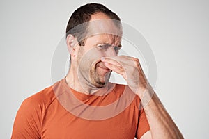 Caucasian man is pinching nose with fingers and looking with disgust because of bad smell isolated on white background