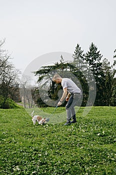 Caucasian man plays toy rope tug-of-war with a dog on green grass. An active spring walk in park of male owner and jack