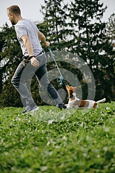 Caucasian man plays toy rope tug-of-war with a dog on green grass. An active spring walk in park of male owner and jack