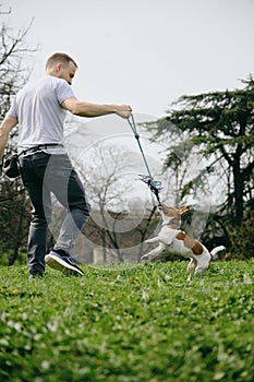 Caucasian man plays toy rope tug-of-war with a dog on green grass. An active spring walk in park of male owner and jack