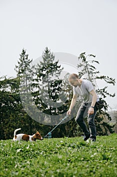 Caucasian man plays toy rope tug-of-war with a dog on green grass. An active spring walk in park of male owner and jack