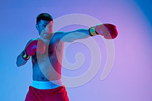 Caucasian man, professional boxer in sportwear boxing on studio background in gradient neon light. Concept of sport