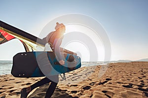 Caucasian man professional surfer standing on the sandy beach with his kite and board