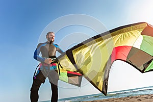 Caucasian man professional surfer standing on the sandy beach with his kite and board