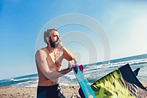 Caucasian man professional surfer standing on the sandy beach with his kite and board on the sandy