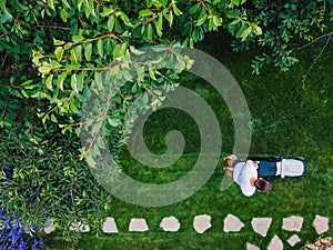 Caucasian man pushing lawn mower for cutting green grass in garden with sunlight at summer season. Aerial view. Housework and