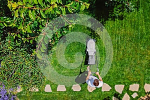 Caucasian man pushing lawn mower for cutting green grass in garden with sunlight at summer season. Aerial view. Housework and