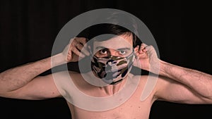 Caucasian man puts on his face a protective mask, khaki, on a black background.