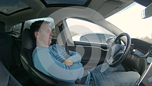 Caucasian man reclines in the driver`s seat of a self steering car during a motorway traffic jam.