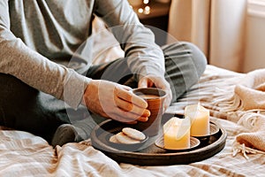 A caucasian man relaxing at home, lighting candle, drinking coffee in bed