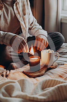 A caucasian man relaxing at home, lighting candle, drinking coffee in bed