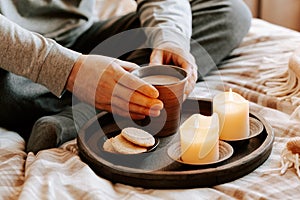 A caucasian man relaxing at home, lighting candle, drinking coffee in bed under blanket