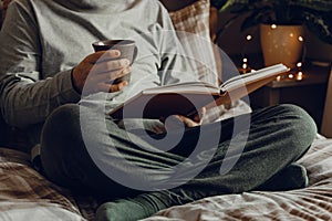 A caucasian man relaxing at home, reading a book, drinking coffee in bed