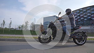 Caucasian man rides an electric motorcycle past a modern building.