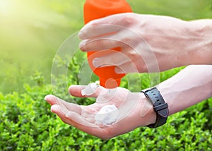 Caucasian man`s male hands applying sun cream sunscreen from plastic container bottle on green background in summer day.