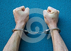 Caucasian man`s wrists in handcuffs against a blue background