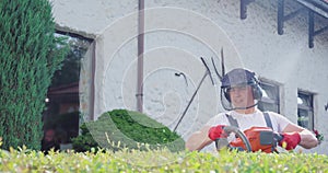 Caucasian man in safety mask and gloves pruning bushes