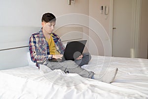 Caucasian man sits in the morning at home on the bed in casual clothes and works at a laptop. Excited man doing online