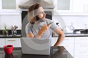 Caucasian man sitting in kitchen using laptop and talking on smartphone