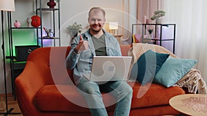 Caucasian man sitting on sofa opening laptop pc starting work e-learning online in room at home