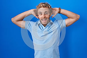 Caucasian man standing over blue background crazy and scared with hands on head, afraid and surprised of shock with open mouth