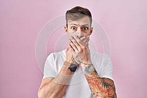 Caucasian man standing over pink background shocked covering mouth with hands for mistake