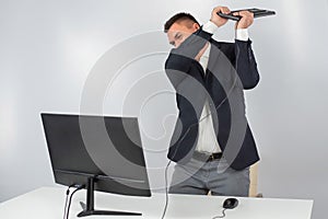 Caucasian man in a suit gets angry and smashes the keyboard on the monitor. An office worker in a rage breaks the