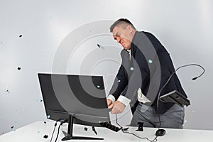 Caucasian man in a suit gets angry and smashes the keyboard on the monitor. An office worker in a rage breaks the