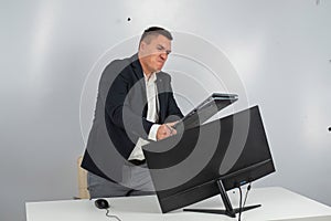 Caucasian man in a suit gets angry and smashes the keyboard on the monitor. An office worker in a rage breaks the