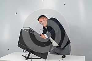 Caucasian man in a suit gets angry and smashes the keyboard on the monitor. An office worker in a rage breaks the