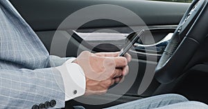 Caucasian man in suit texting message on his cellphone, sitting in car
