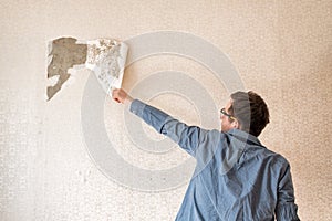 Caucasian man tearing off old wallpaper from wall preparing for home redecoration