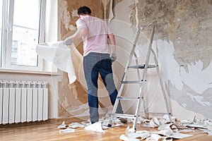 Caucasian man tearing off old wallpaper from wall preparing for home redecoration