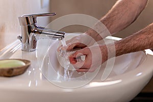 Caucasian man thoroughly cleaning hands and fingernails with a brush in wash basin under running water tap. Personal hygiene