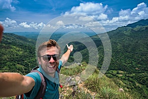 Caucasian man on top of mountain making selfie on background of pretty landscape