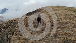 A caucasian man in tourist clothing walks on the top of a plateau next to a deep cliff along with a drone in fog and low