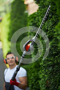 Caucasian man trimming hedge with petrol cutter.