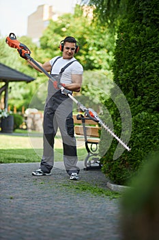 Caucasian man in uniform shaping hedge with electric trimmer