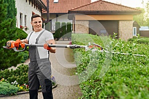 Caucasian man in uniform trimming bushes at garden