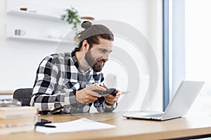 Caucasian man using joystick and laptop sitting at wooden table at kitchen.