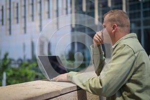 Caucasian man using laptop outdoors against building background.