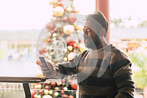 Caucasian man using mobile phone in winter christmas period with tree in background at commercial mall center for shopping and buy photo