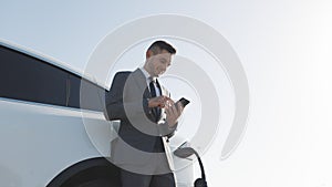 Caucasian man using smart phone and waiting power supply connect to electric vehicles for charging the battery in car