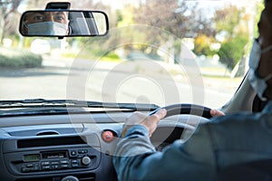 Caucasian man wearing face mask and driving and looking thorough the rear view mirror of the car. Covid-19