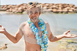 Caucasian man wearing hawaiian lei at the beach celebrating achievement with happy smile and winner expression with raised hand