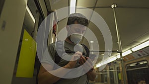 A Caucasian man wearing protective mask uses smartphone while standing at the door of a vintage subway train in Munich