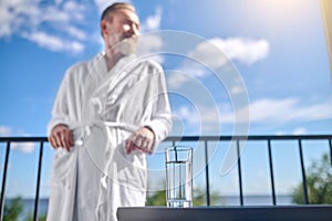Caucasian man in a white bathrobe standing on the balcony