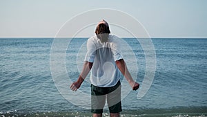 Caucasian man in white shirt stands against background of calm blue sea and stretches.